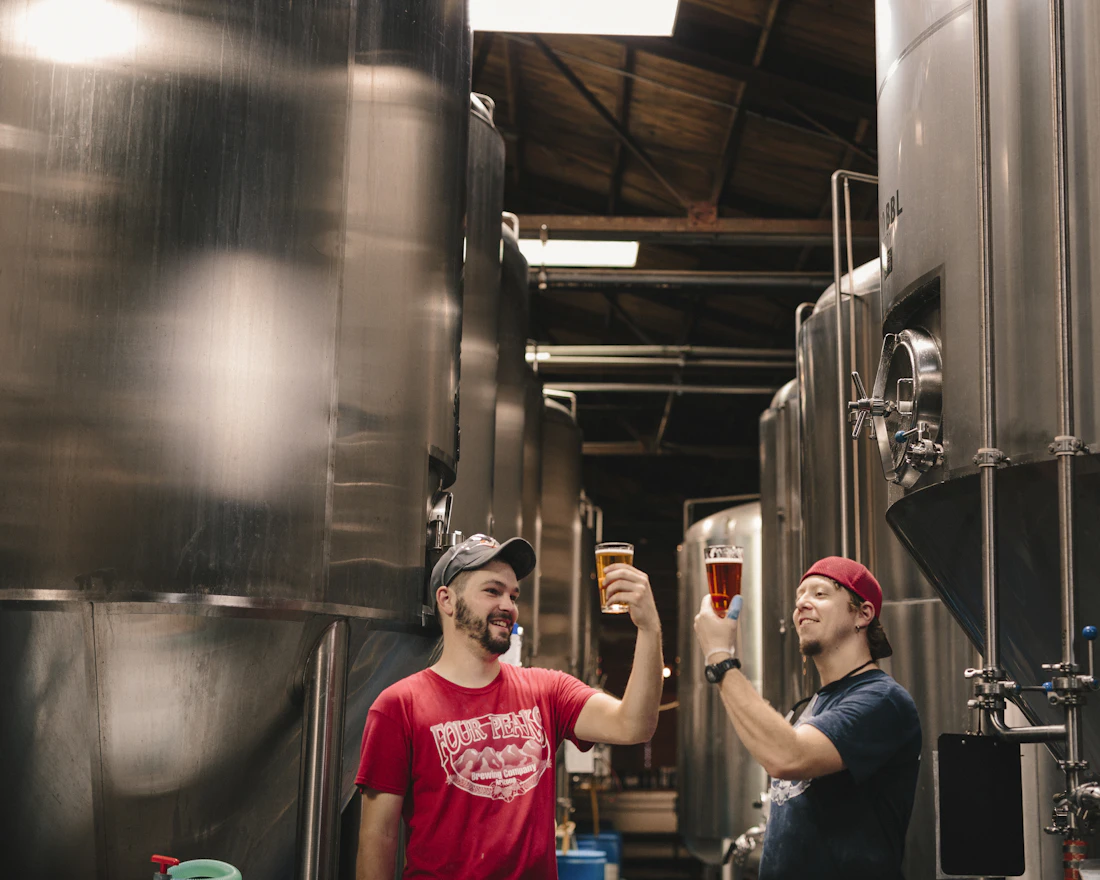 Two brewers tasting beer next to the tanks